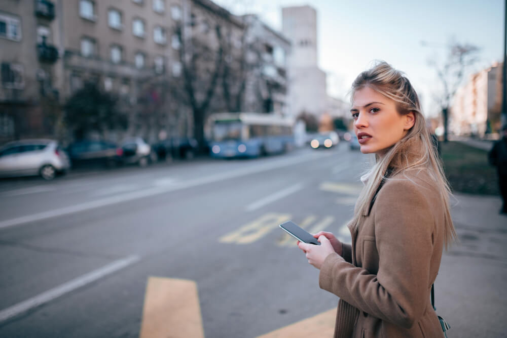 Visitor holding a smartphone on a central London street, looking uncertain about navigation directions
