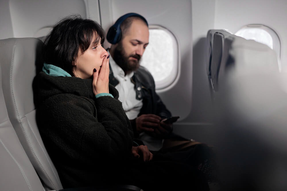Anxious passenger on board an aircraft looking out the window with another passenger beside them using a phone during a flight