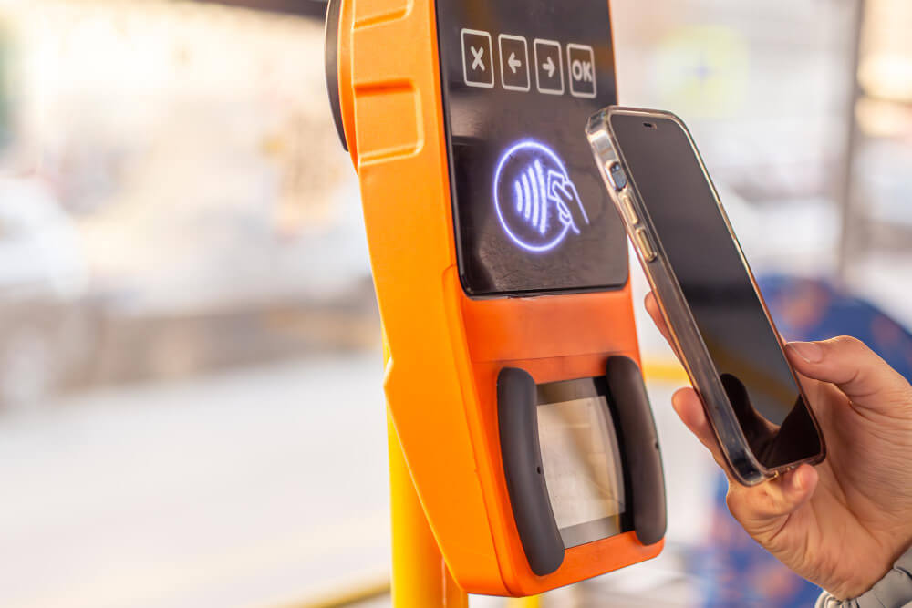 Smartphone being tapped against a contactless payment reader on public transport, showing the NFC payment symbol