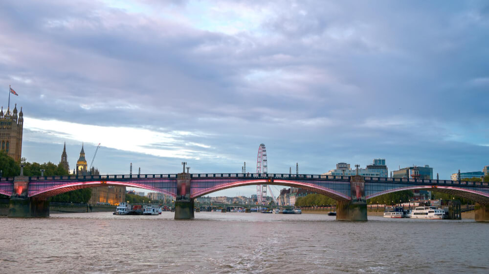 Westminster Bridge over the River Thames with the London Eye and County Hall on the South Bank, a river cruise passing beneath in autumn light
