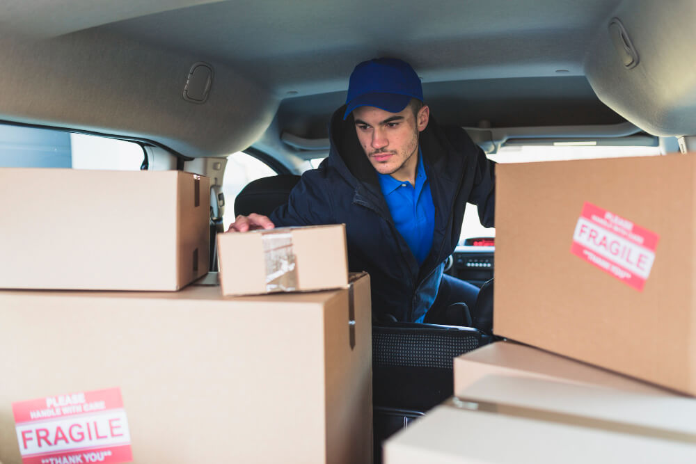 Driver carefully loading fragile-labelled packages into a vehicle boot, demonstrating the careful handling required for antiques and valuables during airport transfers