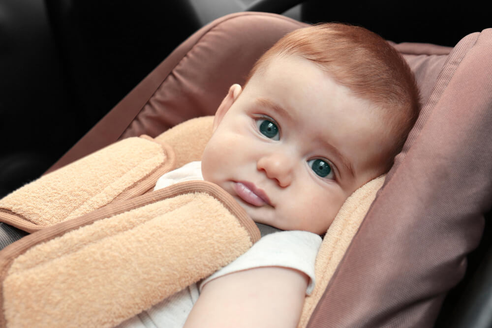 Newborn baby secured in a rear-facing infant carrier with padded harness straps, ready for a safe first journey